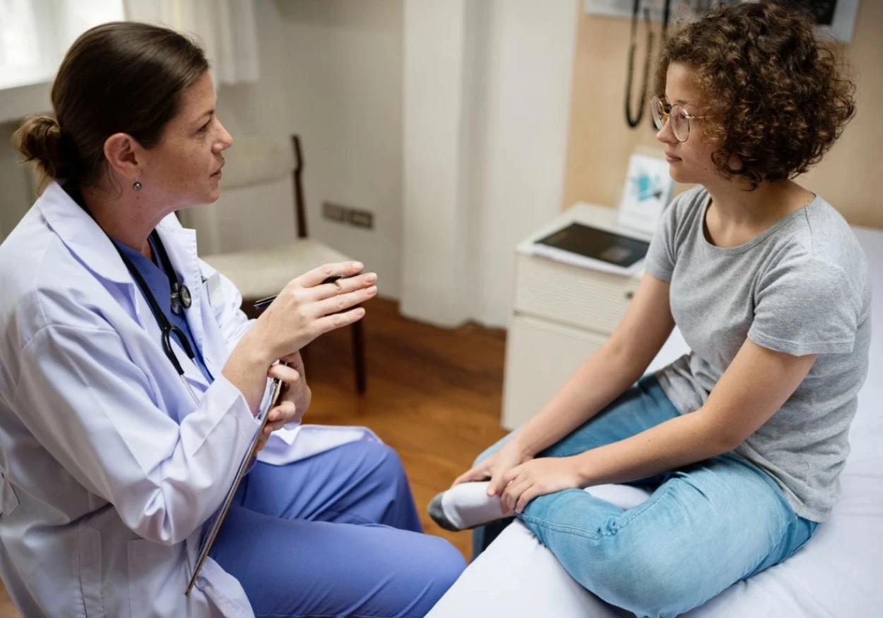 A doctor sits with a young patient in discussion.