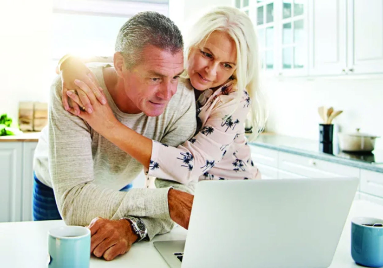 A couple looking at a laptop in the kitchen.