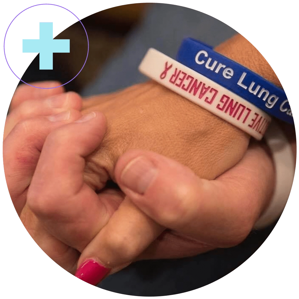 Two hands holding each other wearing cure lung cancer wrist bands.