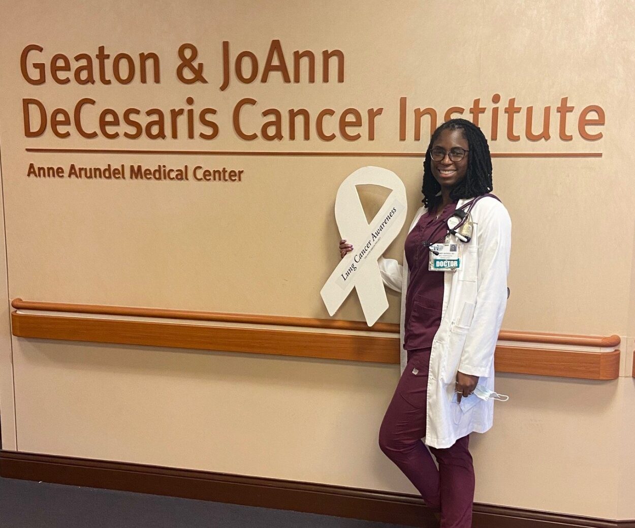 Dr. Sydney Barned in front of the Geaton & JoAnn DeCesaris Cancer Institute sign.