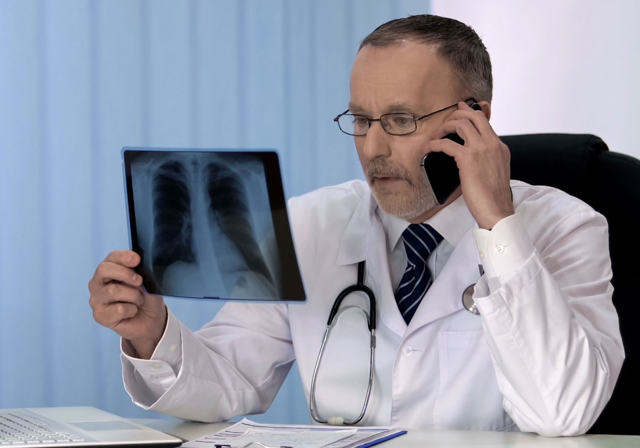 A doctor talks on the phone while holding an x-ray.